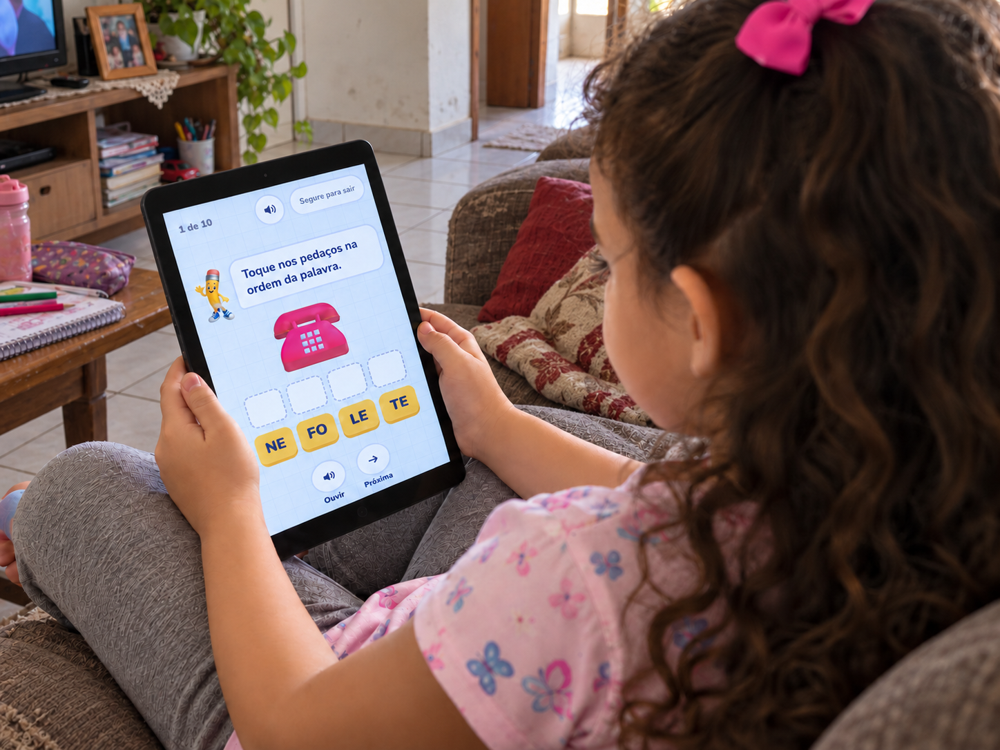 Criança no sofá usando uma atividade de montagem de palavras do Trilha das Letras em um tablet.